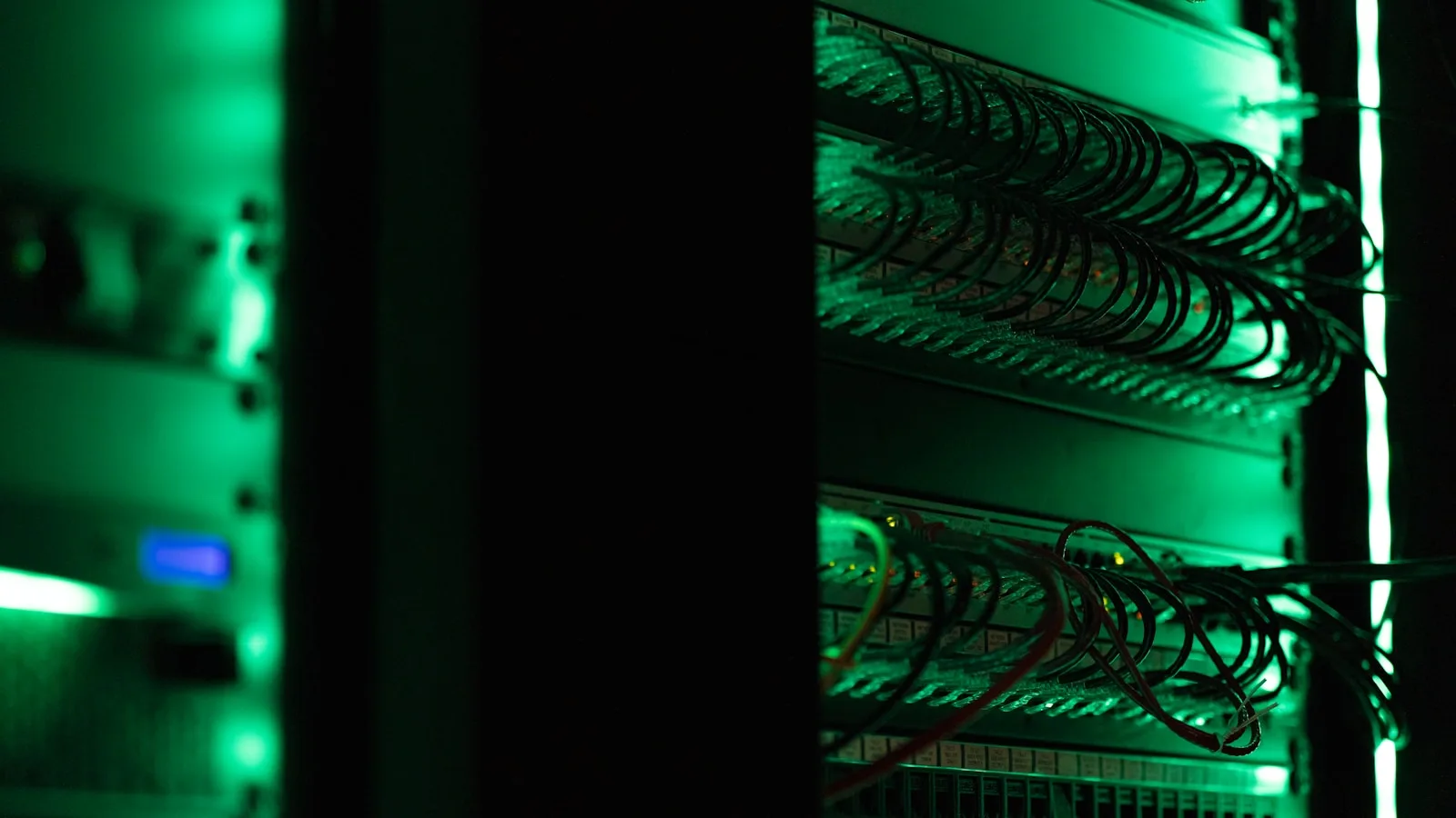 Primer plano de un rack de servidores en una sala de datos en penumbra, con haces de cables de red iluminados en verde