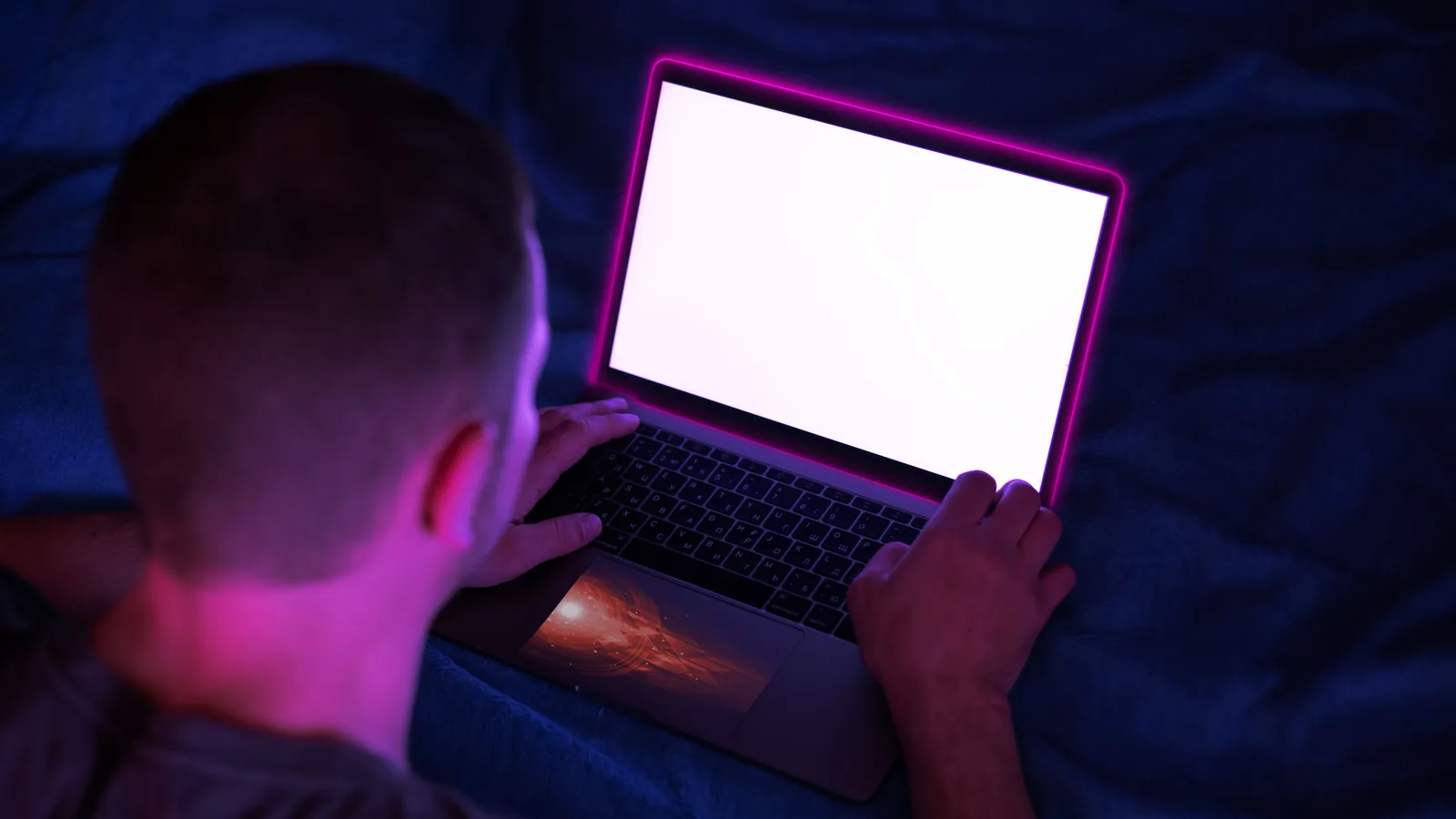 Persona vista desde atrás trabajando con un portátil iluminado en una habitación oscura