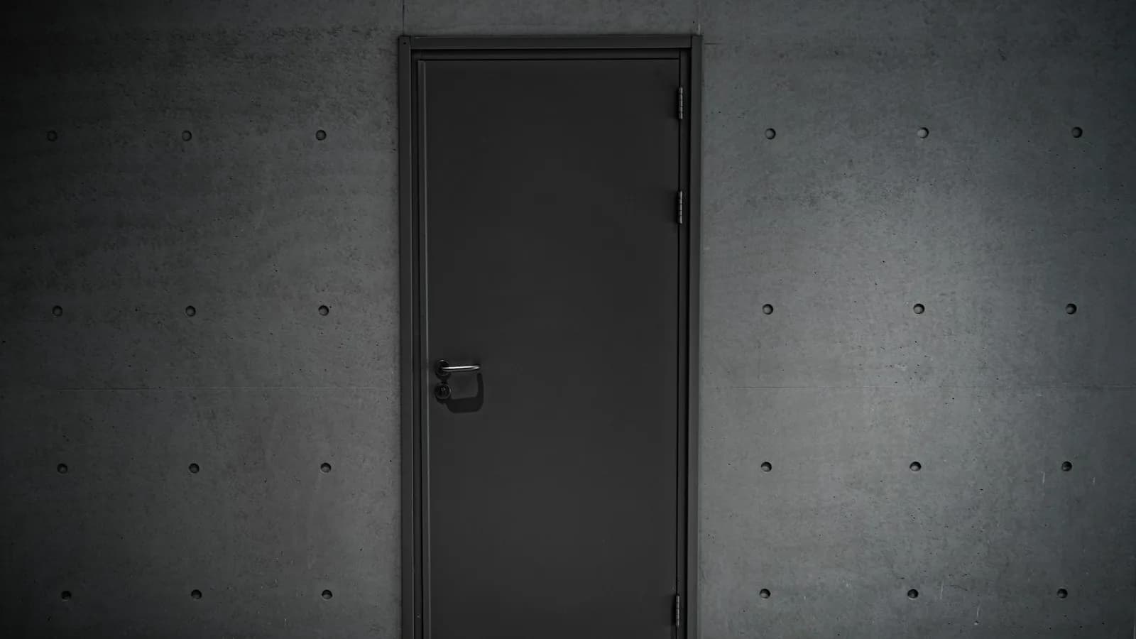 Puerta metálica cerrada en un muro de hormigón visto, apenas iluminada