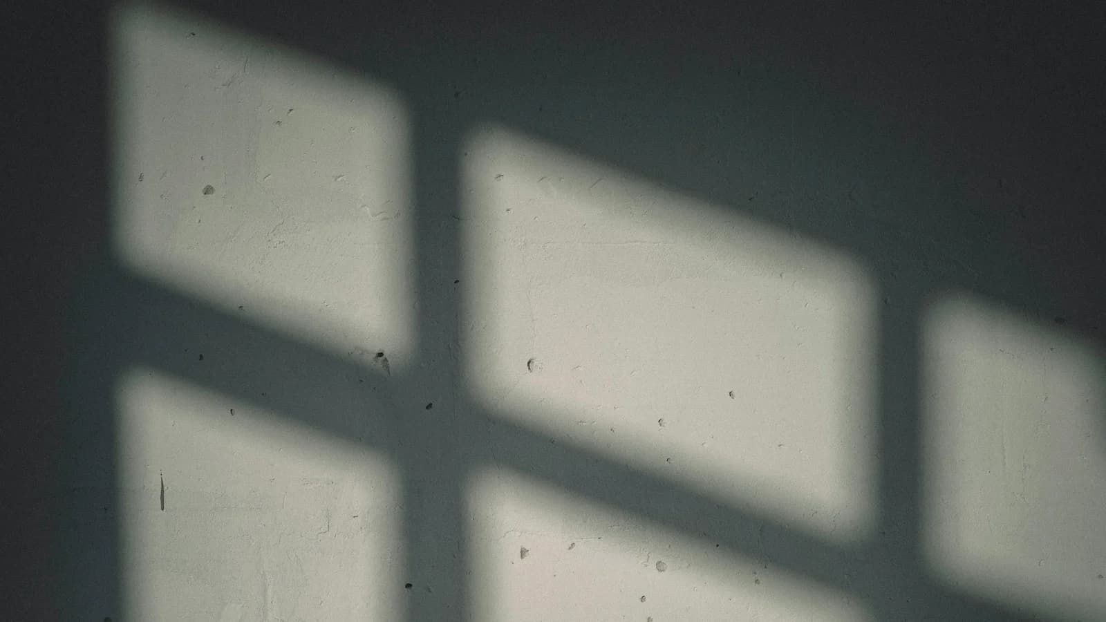 Luz de una ventana proyectada sobre una pared gris verdosa, entre amplias zonas de sombra.