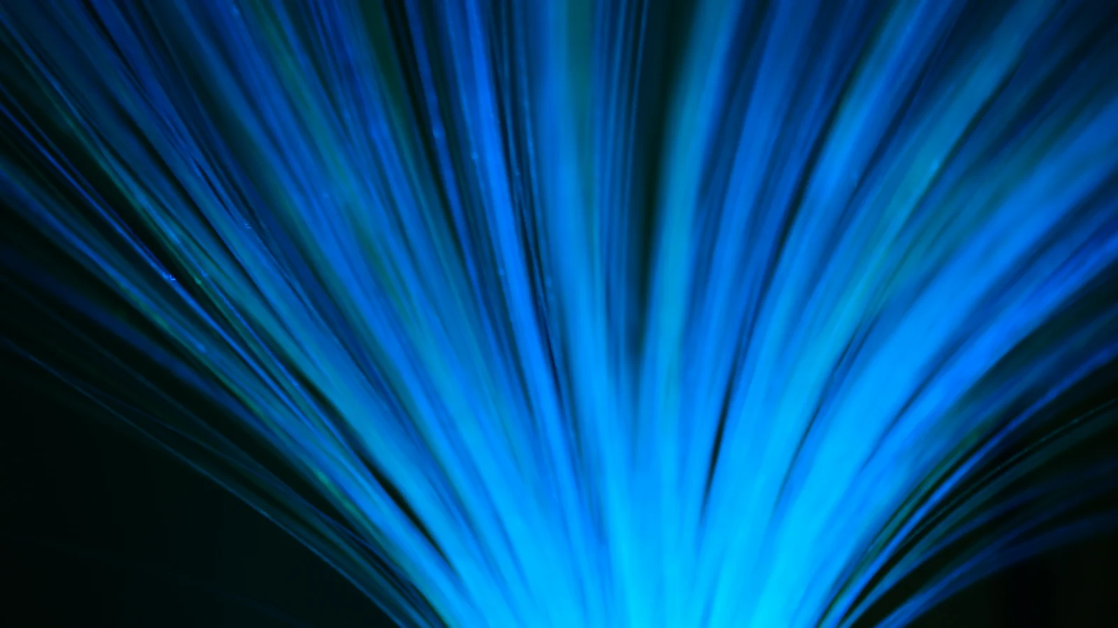 Haces de fibra óptica azul y verde sobre un fondo negro, vistos en perspectiva radial.