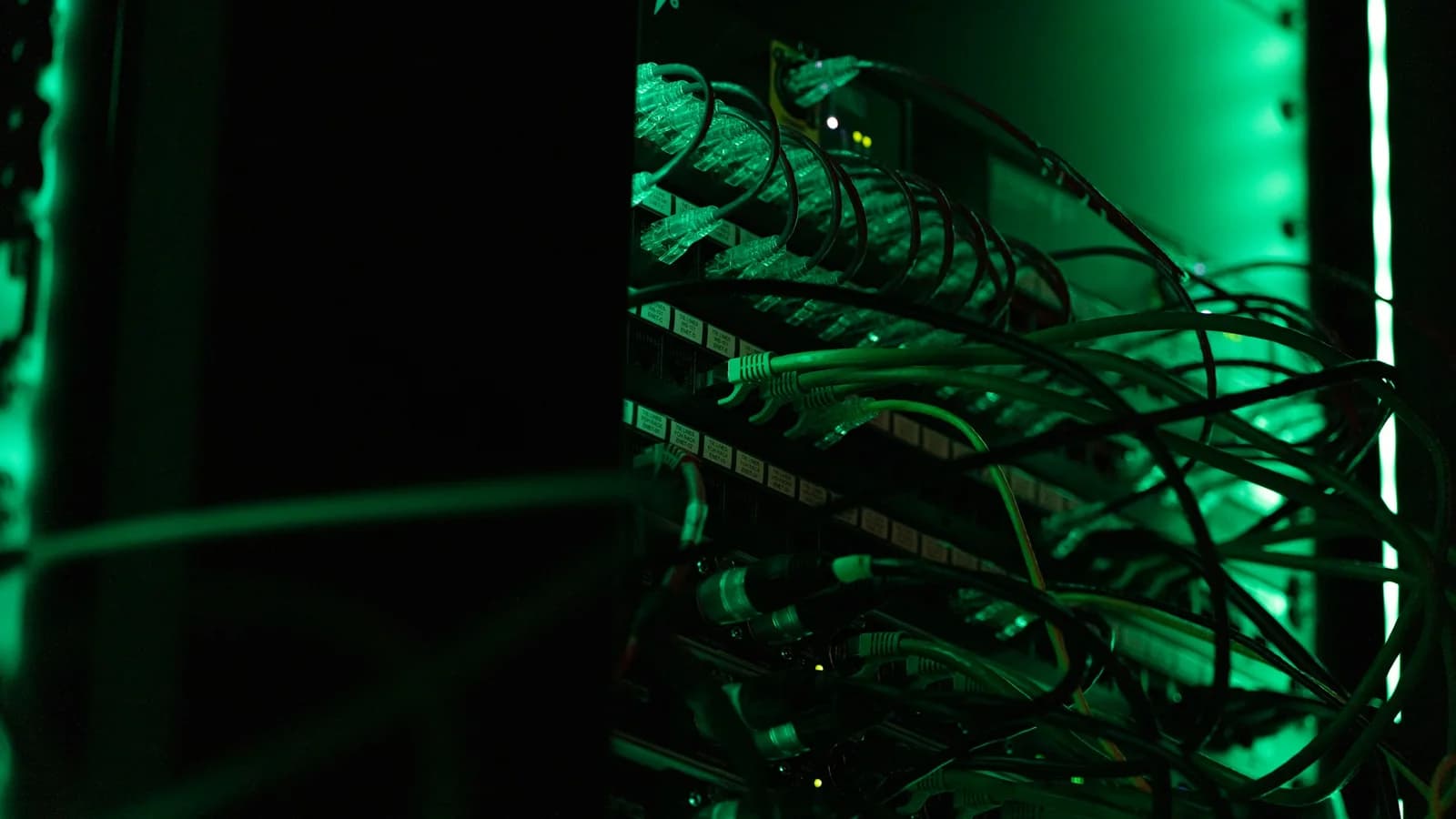 Panel de conexiones de red iluminado en verde dentro de un armario técnico oscuro.