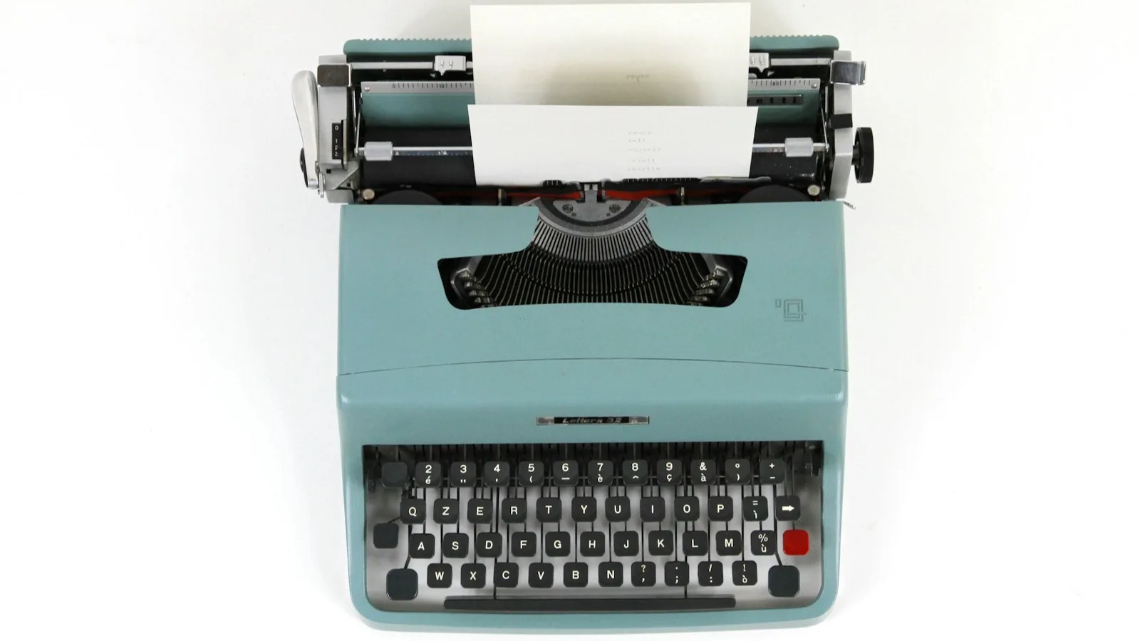 Máquina de escribir vintage de color turquesa vista desde arriba, con una hoja de papel a medio escribir