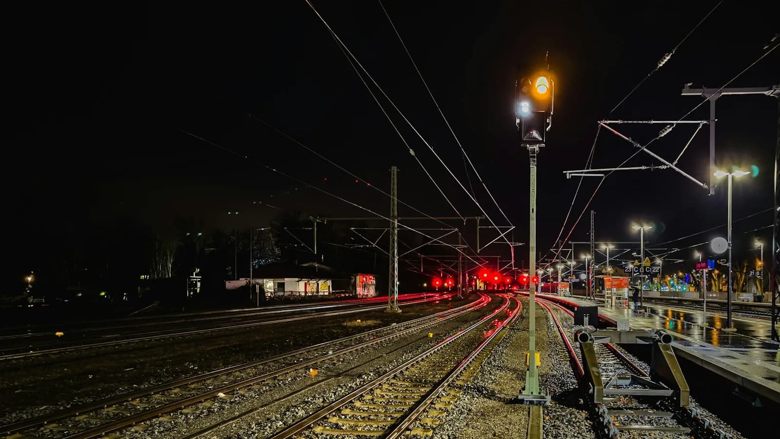 Haz de vías férreas de noche con varias señales luminosas en rojo y una torre de señalización en primer plano