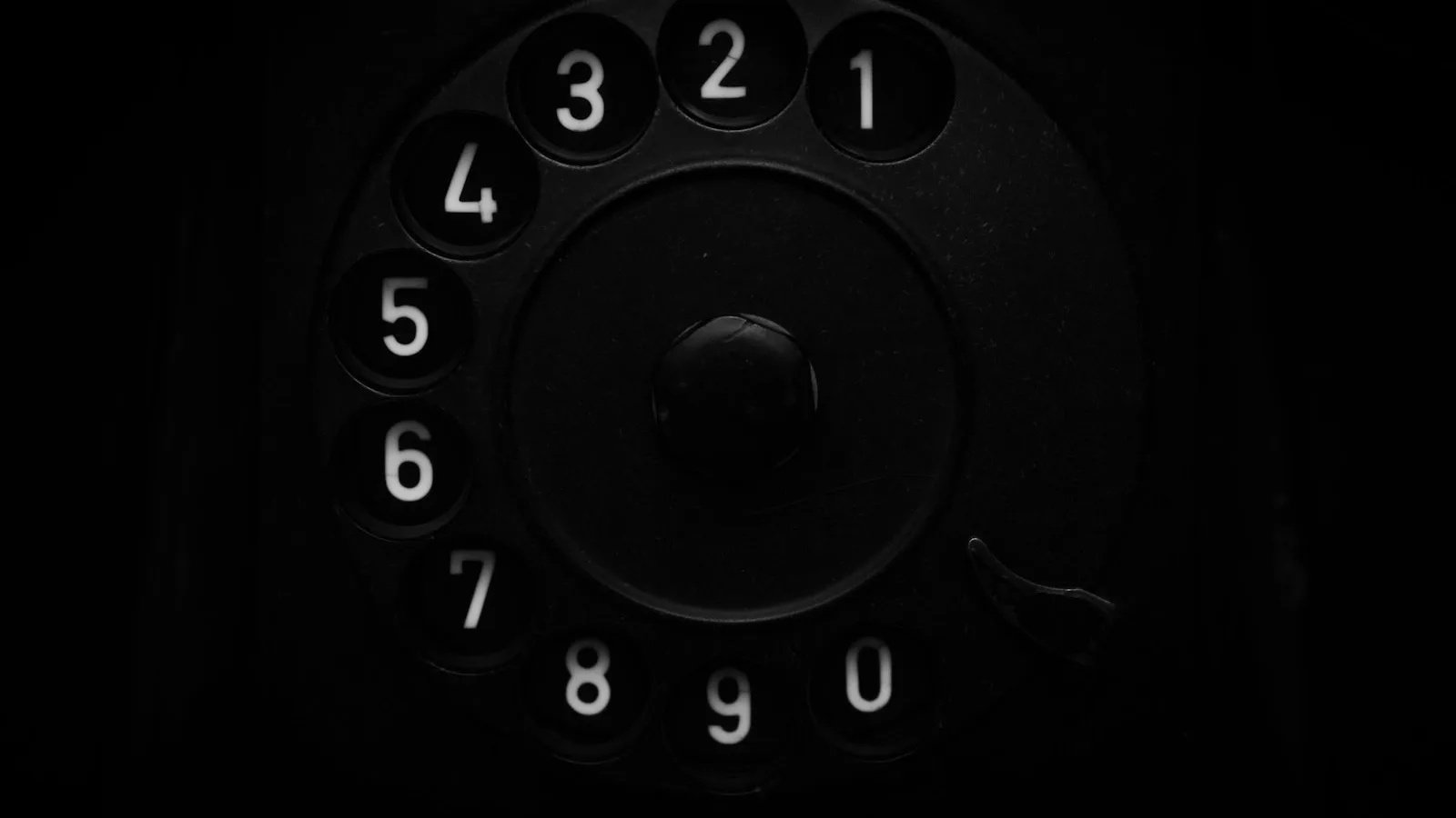 Primer plano en blanco y negro del disco numerado de un teléfono antiguo de baquelita, en penumbra