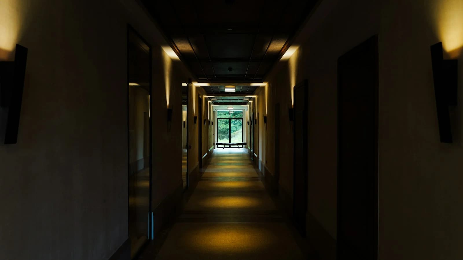 Pasillo de hotel vacío y en penumbra, con puertas a ambos lados y luz natural al fondo