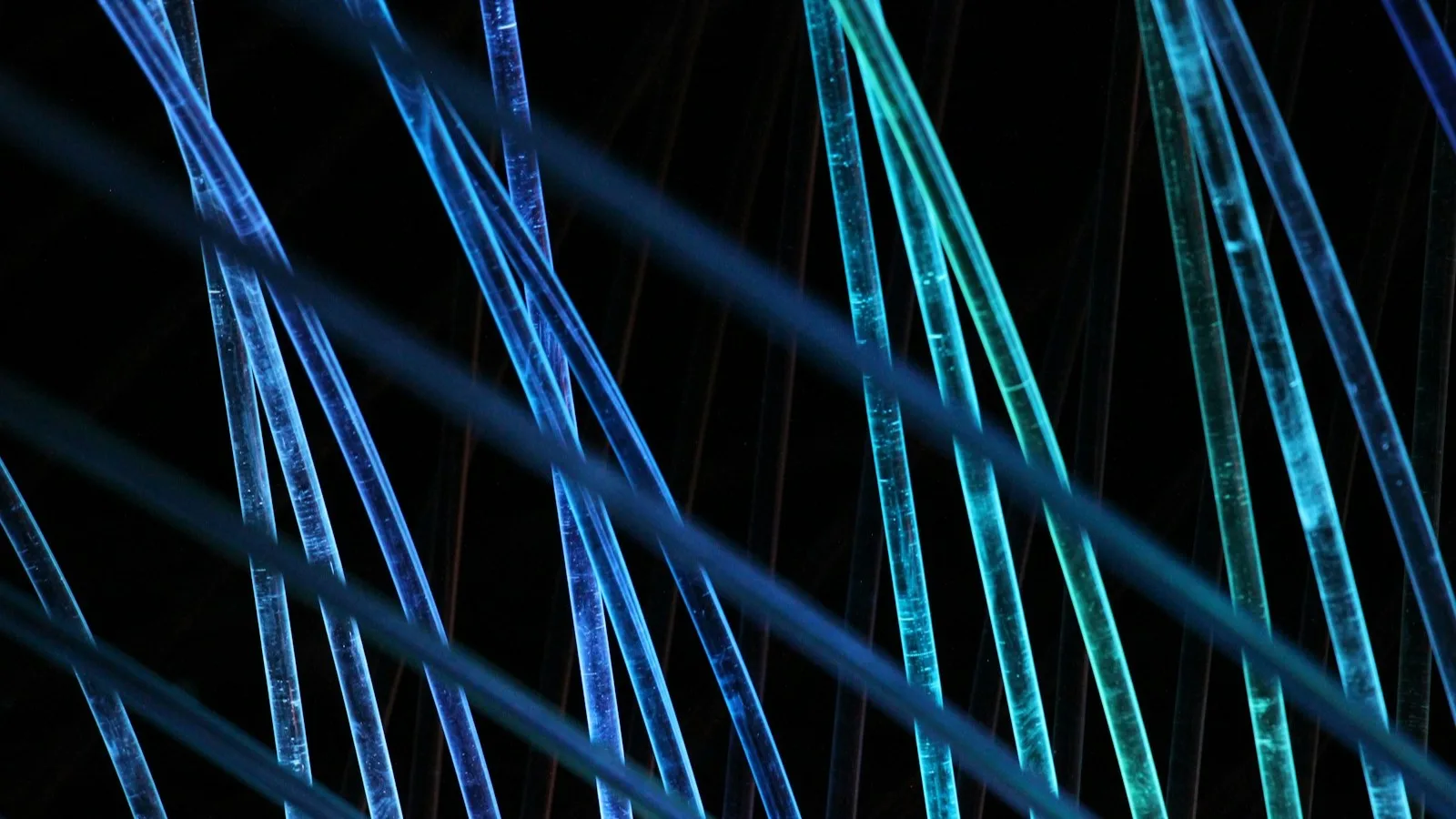 Primer plano de hilos de fibra óptica iluminados en azul y verde cruzándose sobre un fondo negro