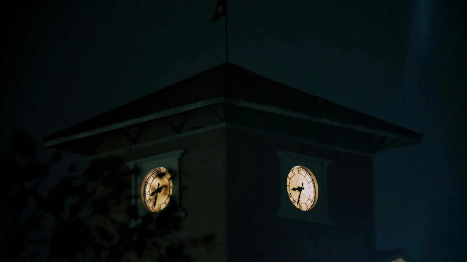 Torre de reloj universitaria iluminada de noche, con las esferas del reloj brillando contra un cielo oscuro
