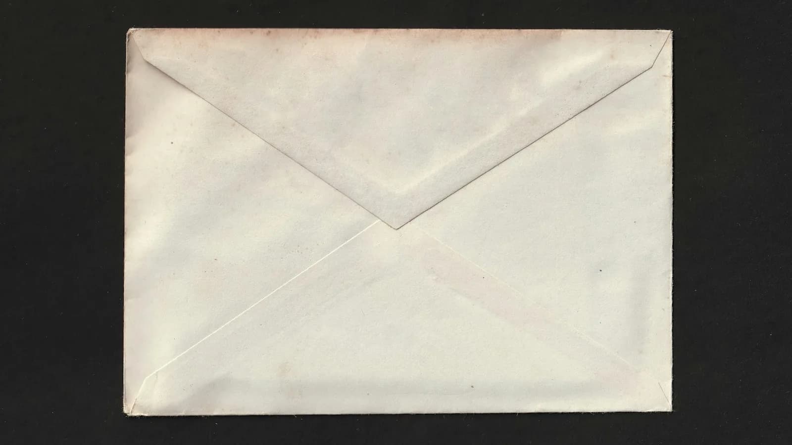 Sobre de papel cerrado sobre fondo negro, visto por su parte trasera