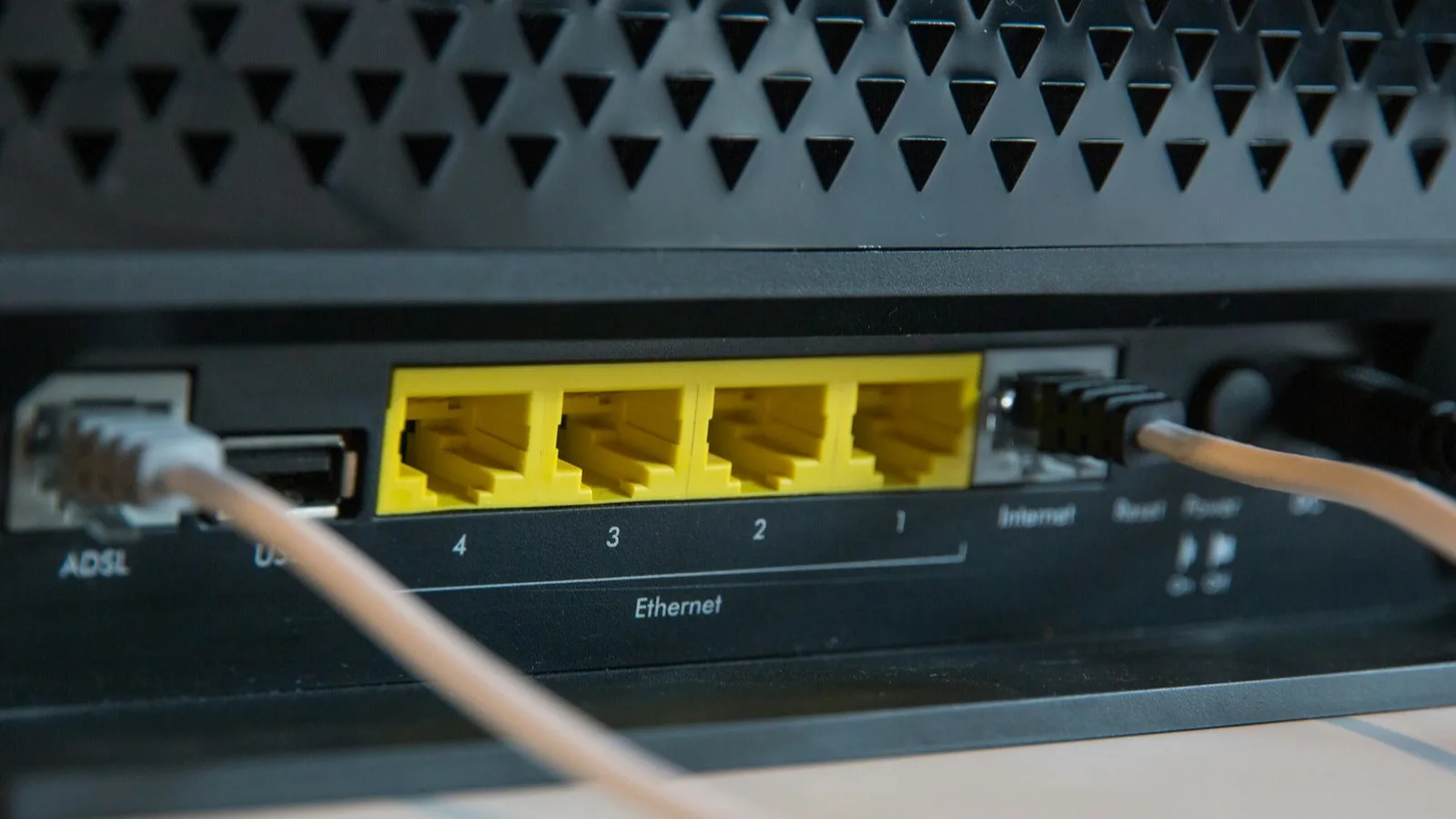 Panel trasero de un router doméstico con los puertos Ethernet iluminados en amarillo y cables conectados, sobre un fondo oscuro