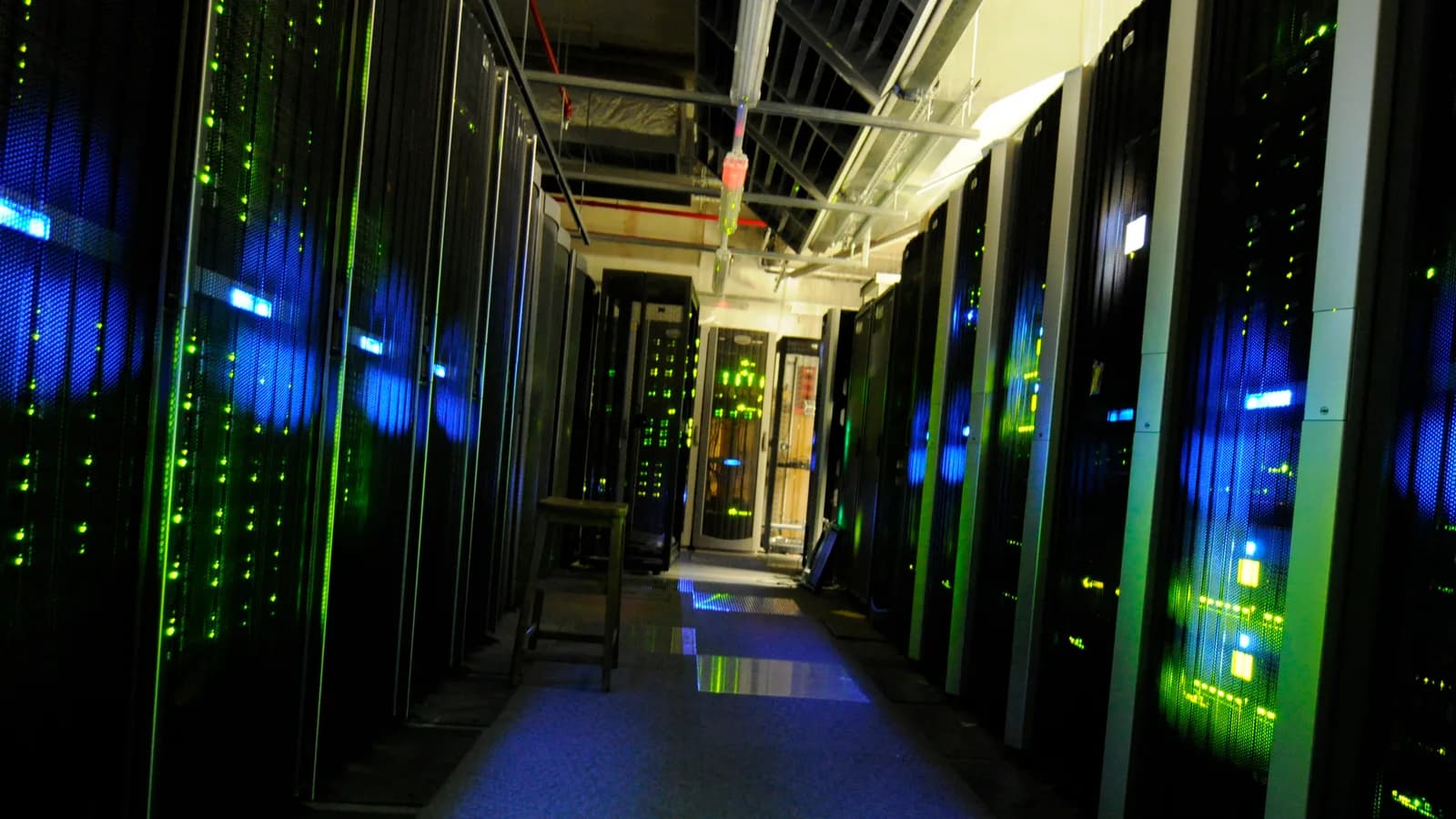 Pasillo oscuro entre racks de servidores iluminados por indicadores verdes y azules.