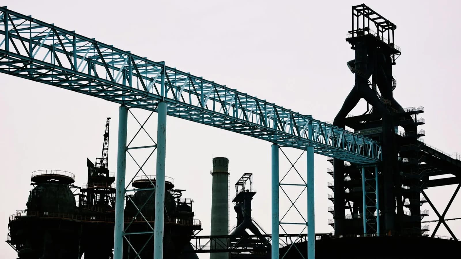Silueta a contraluz de una planta industrial con una pasarela de cinta transportadora elevada cruzando la imagen