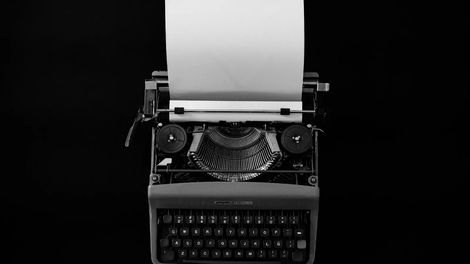Máquina de escribir vintage en blanco y negro sobre fondo negro, con una hoja en blanco asomando por el rodillo